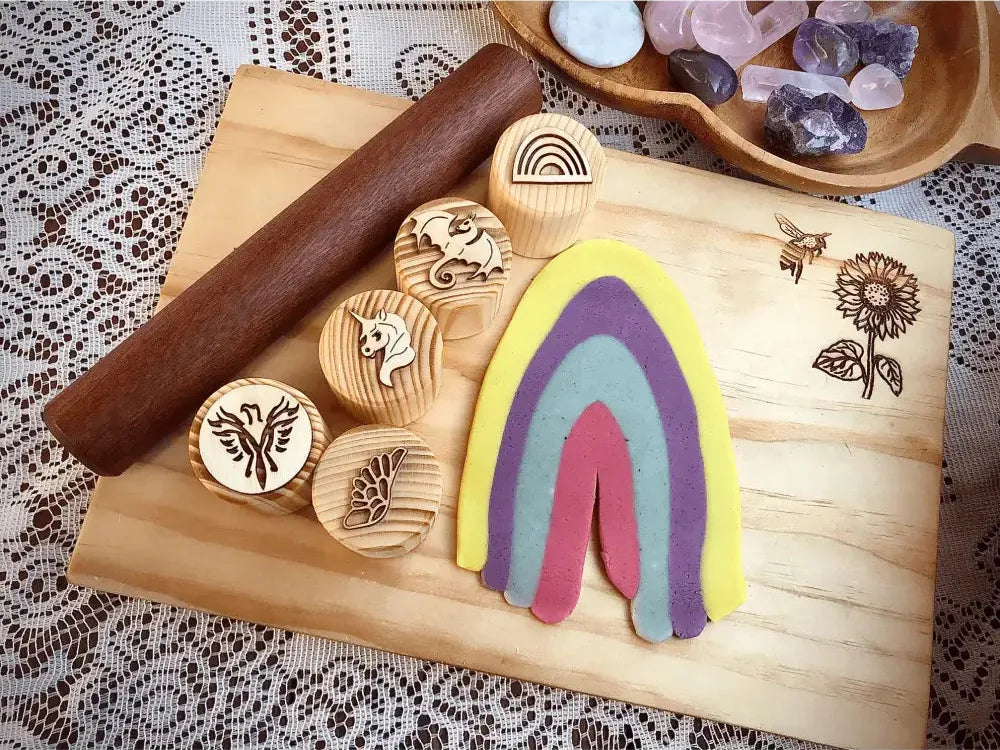 Colorful rainbow-shaped clay or playdough sculpture on a wooden board with wooden stamps nearby.