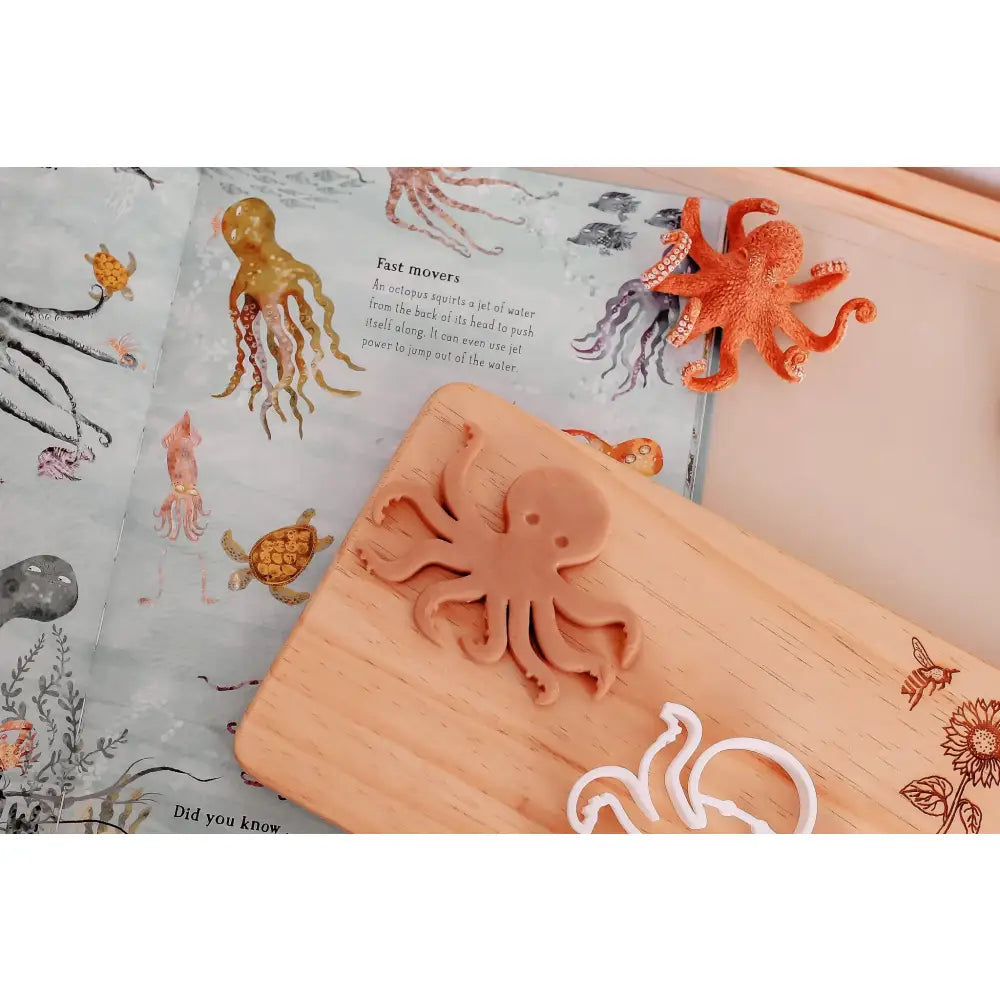 Wooden cutting board with an octopus-shaped cookie cutter on top.