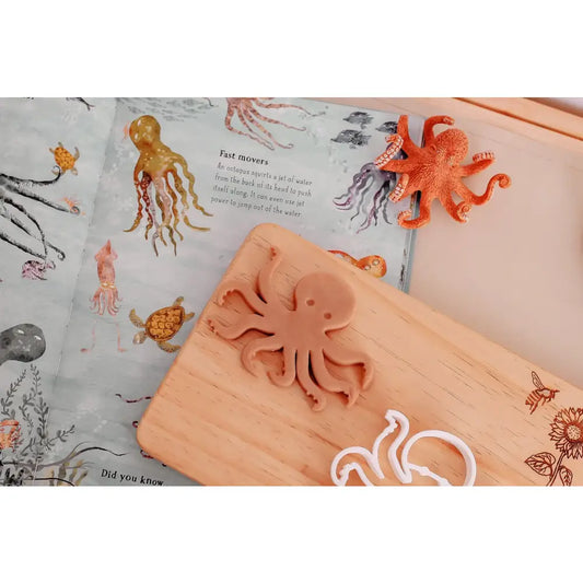 Wooden cutting board with an octopus-shaped cookie cutter on top.