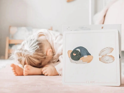 Child lying face-down on a pink surface next to a card with illustrated shapes.