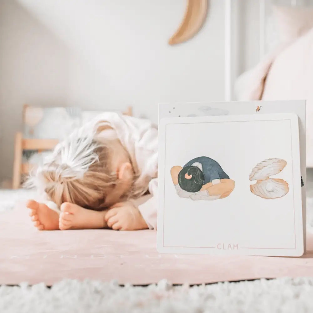 Child lying face-down on a pink surface next to a card with illustrated shapes.