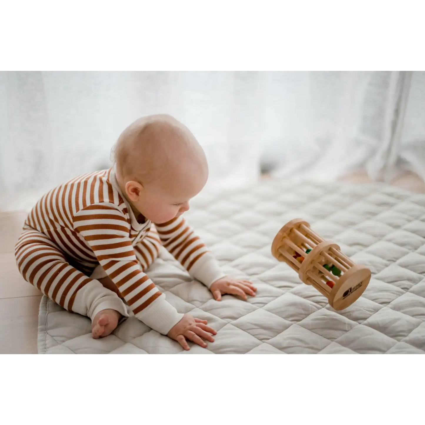 Baby in striped clothing playing with a wooden toy on a bed.
