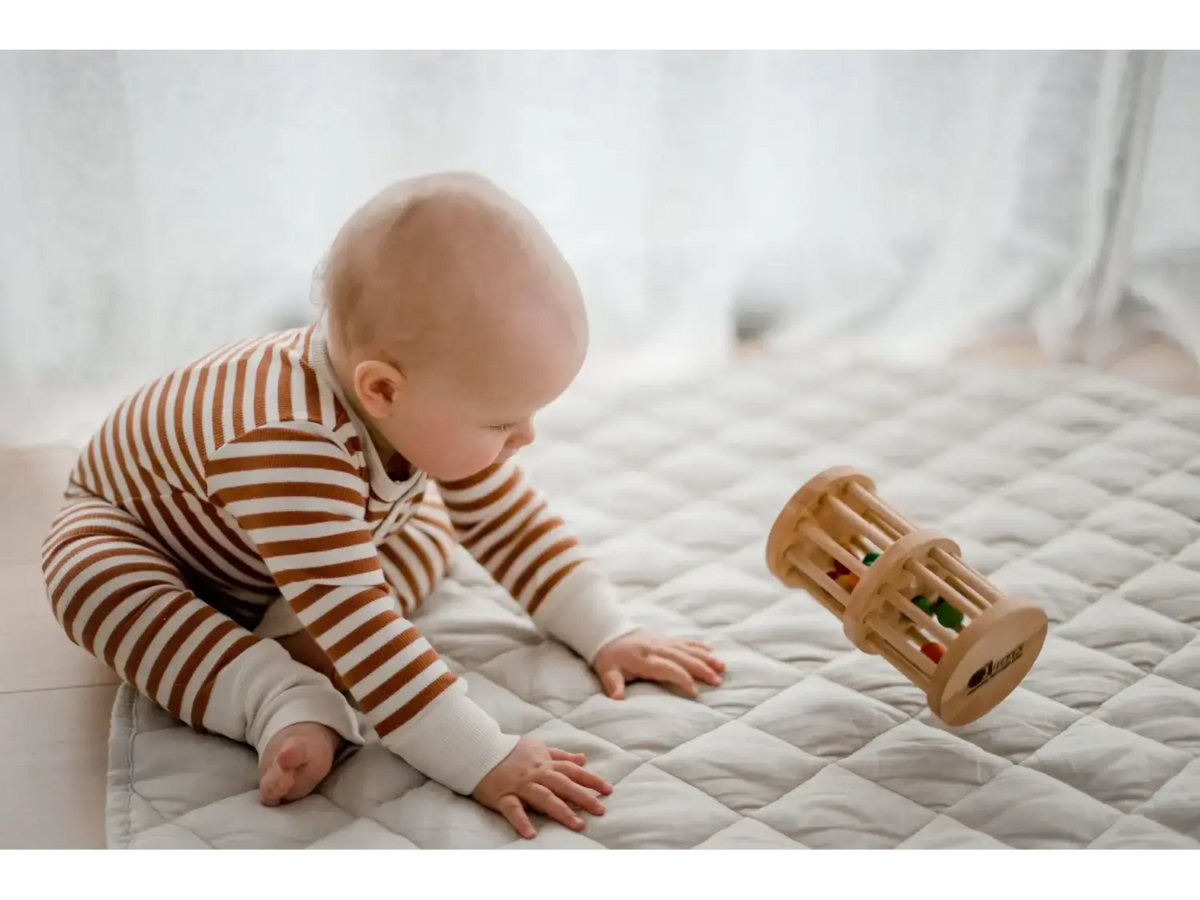 Baby in striped clothing playing with a wooden toy on a bed.