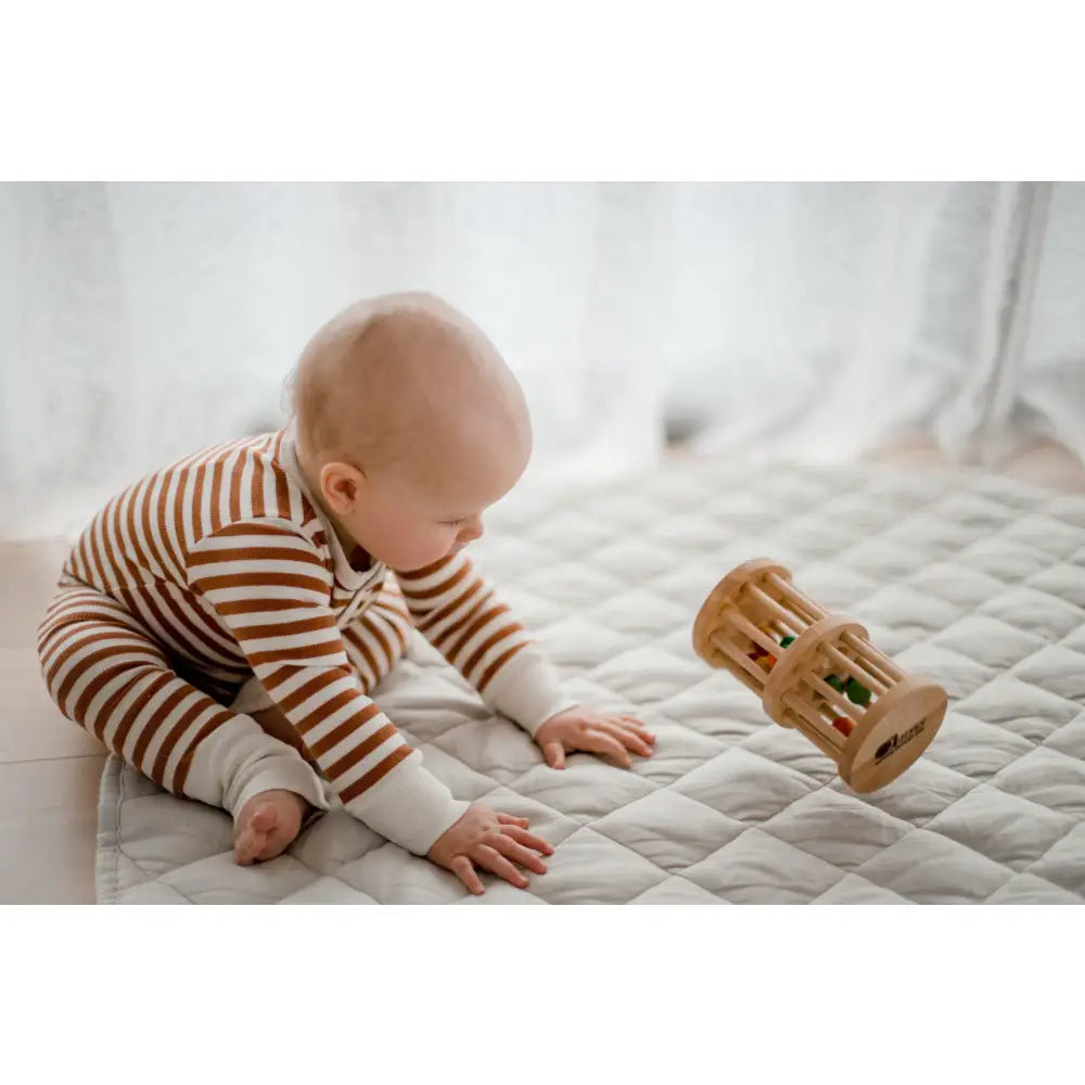 Baby in striped clothing playing with a wooden toy on a bed.