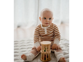 Baby wearing striped clothing sitting on a bed with a wooden toy.