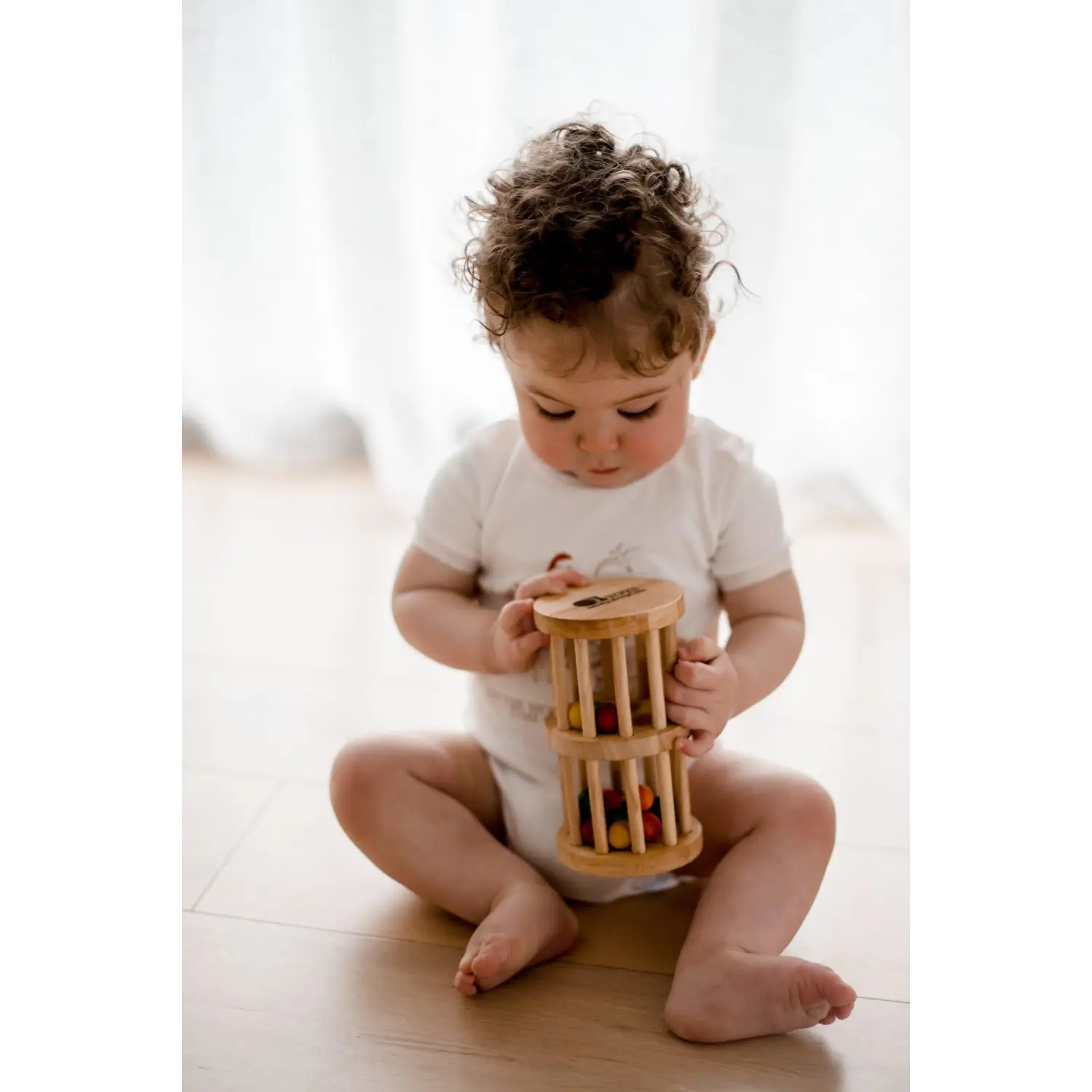Toddler sitting on a floor playing with a wooden cylinder toy.