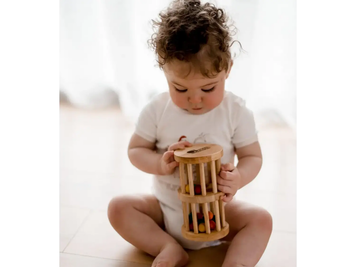 Toddler sitting on a floor playing with a wooden cylinder toy.
