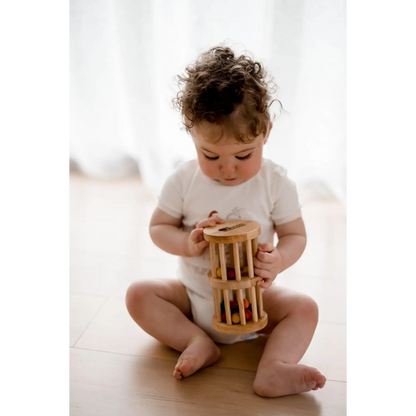 Toddler sitting on a floor playing with a wooden cylinder toy.