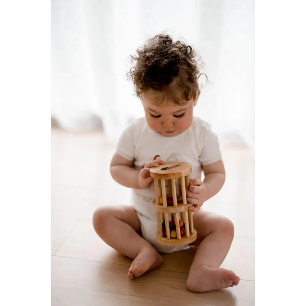 Toddler sitting on a floor playing with a wooden cylinder toy.