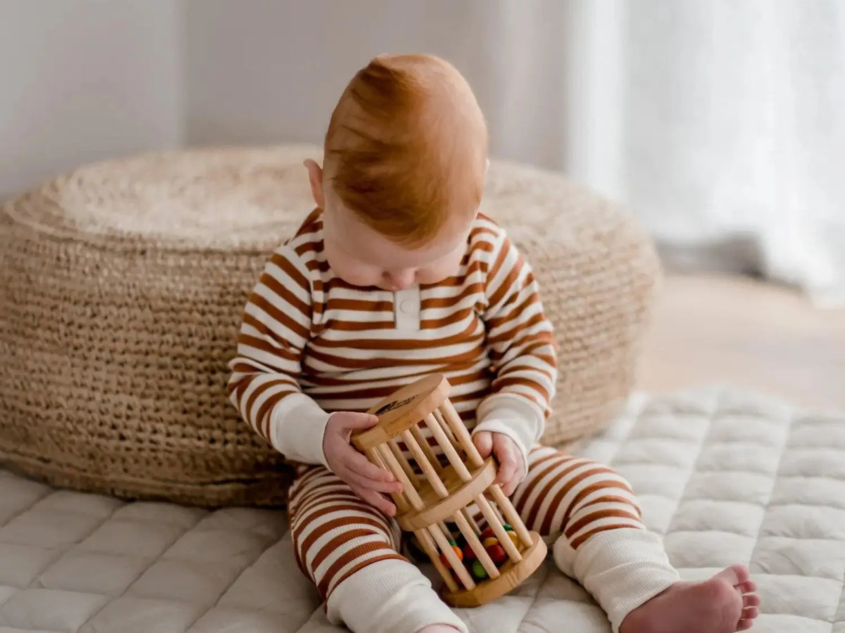 Baby wearing striped pajamas playing with a wooden toy.