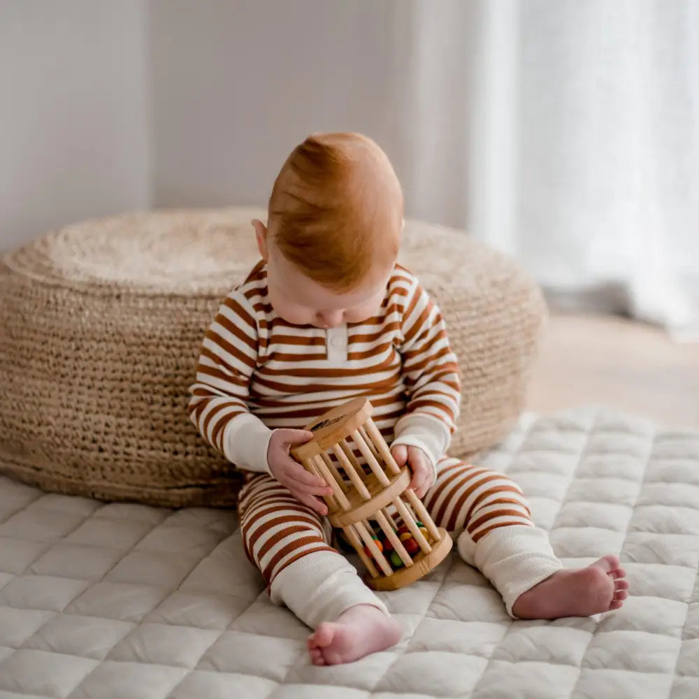 Baby wearing striped pajamas playing with a wooden toy.