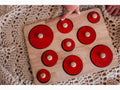 Wooden puzzle board with red circular pieces of varying sizes.