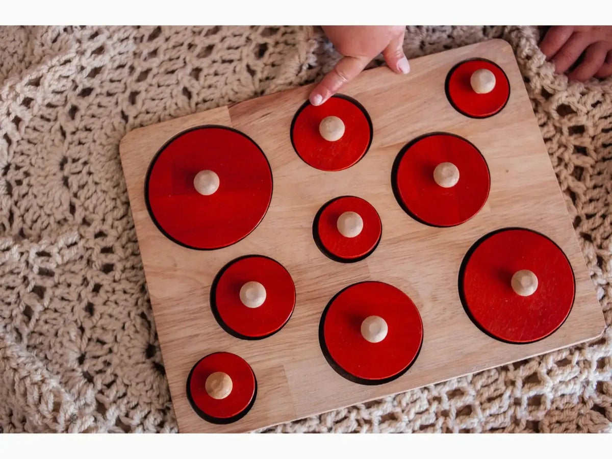 Wooden puzzle board with red circular pieces of varying sizes.