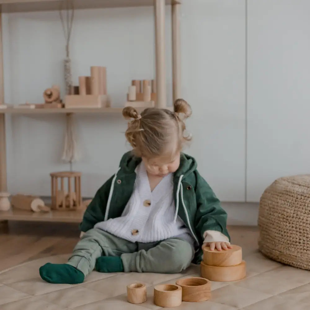 Young child sitting on the floor playing with wooden toys.