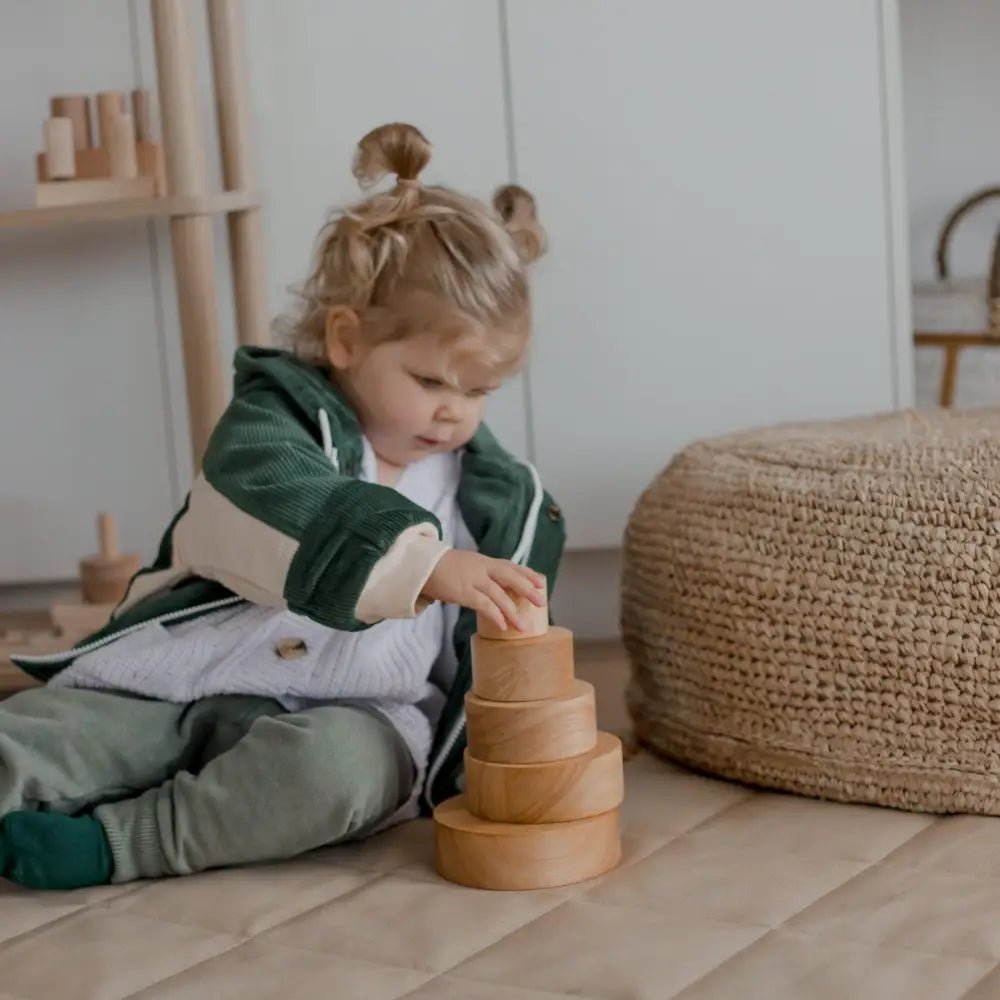 Child playing with a wooden stacking toy on the floor.