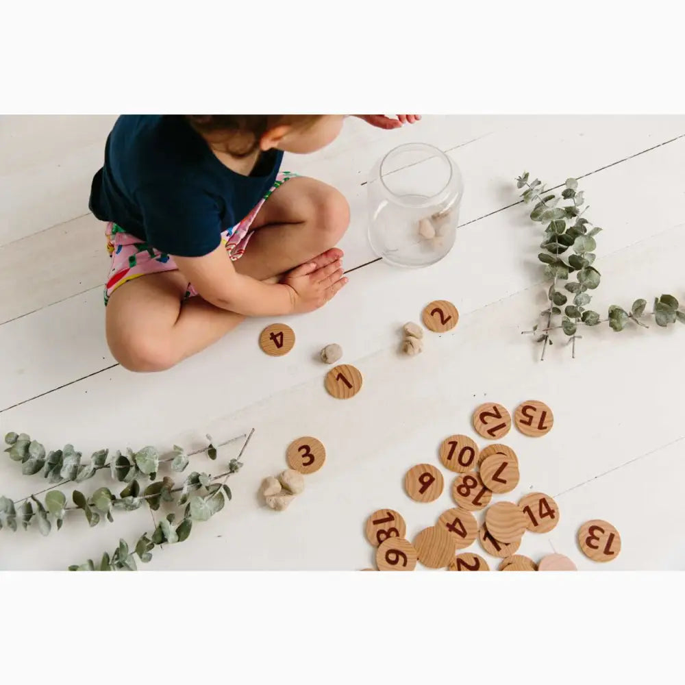 Wooden number tokens scattered on a white floor alongside eucalyptus branches.