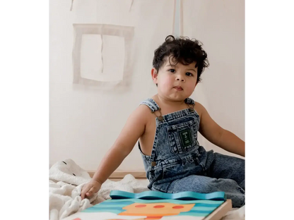 Child wearing denim overalls sitting on the floor with a colorful board game or puzzle.