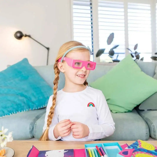 Young girl wearing bright pink glasses and a white shirt with a rainbow design.
