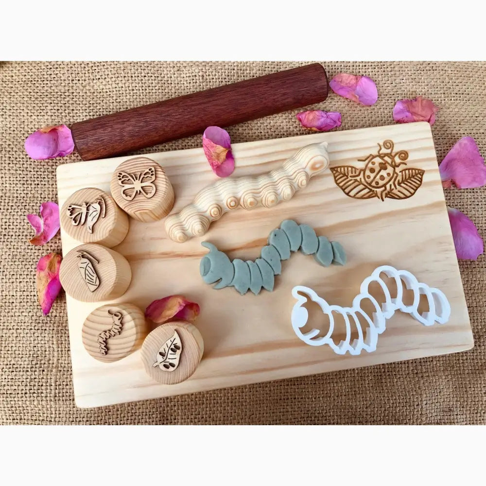 Wooden board displaying various handmade stamps, clay shapes, and pink flower petals.