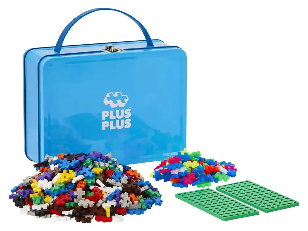 Blue metal lunchbox-style container with ’PLUS PLUS’ logo, accompanied by colorful plastic building blocks and a green baseplate.