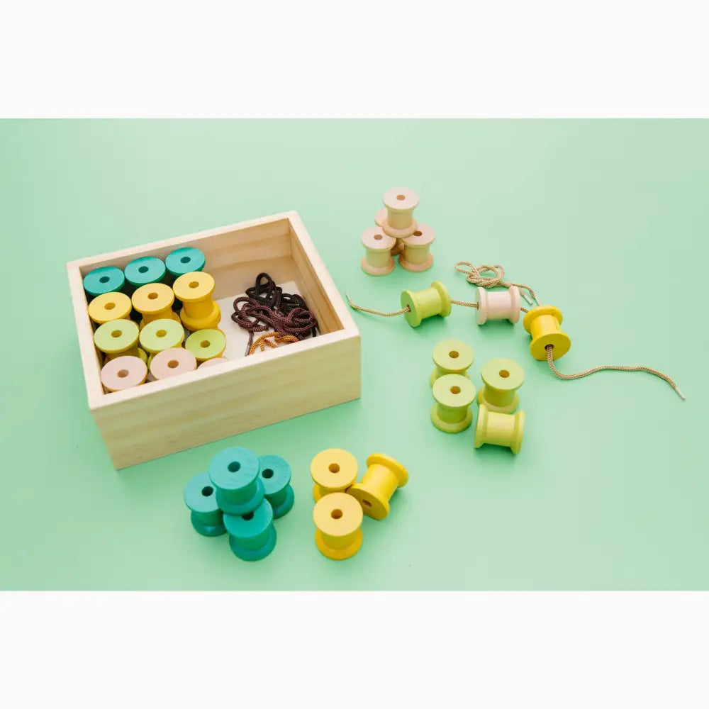 Wooden box containing colorful wooden spools and beads for threading or crafting.