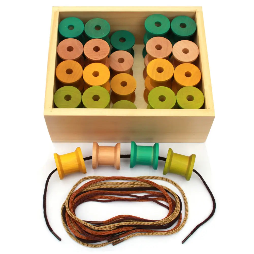 Wooden box containing colorful cylindrical beads with holes, accompanied by spools and laces for threading.