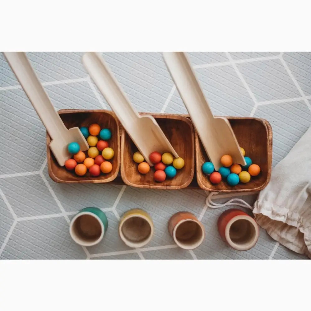 Wooden trays filled with colorful wooden balls alongside small ceramic cups.