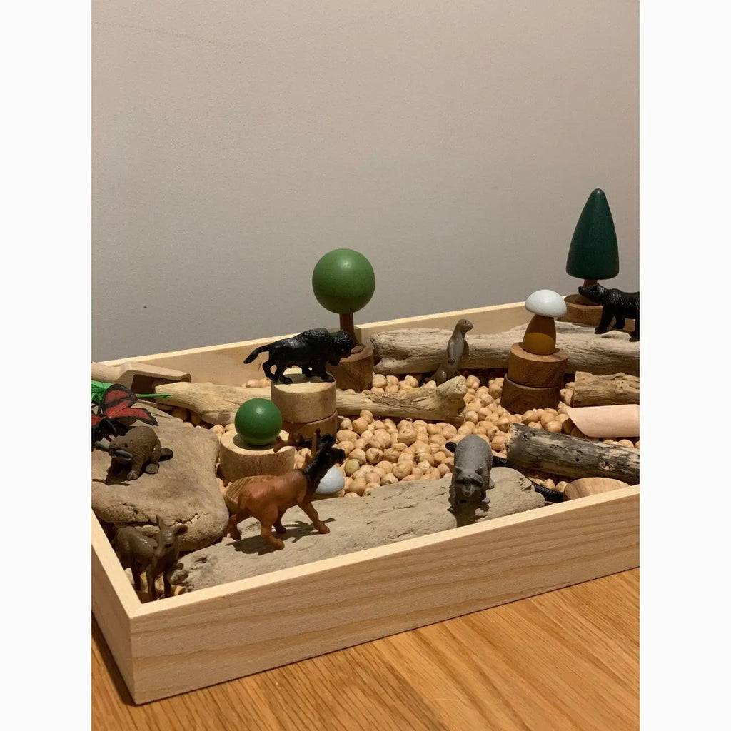 Wooden sandbox or play tray filled with miniature animals, trees, and natural elements.