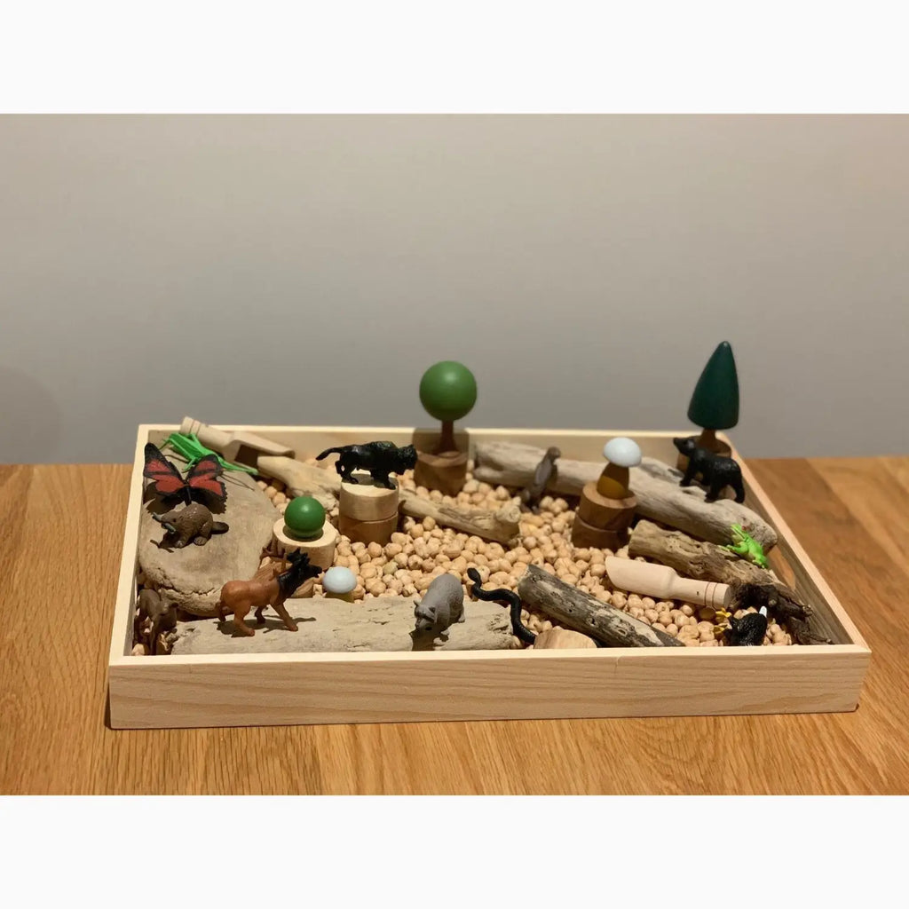 Wooden tray filled with miniature animal figurines, trees, and pebbles creating a small-scale nature scene.