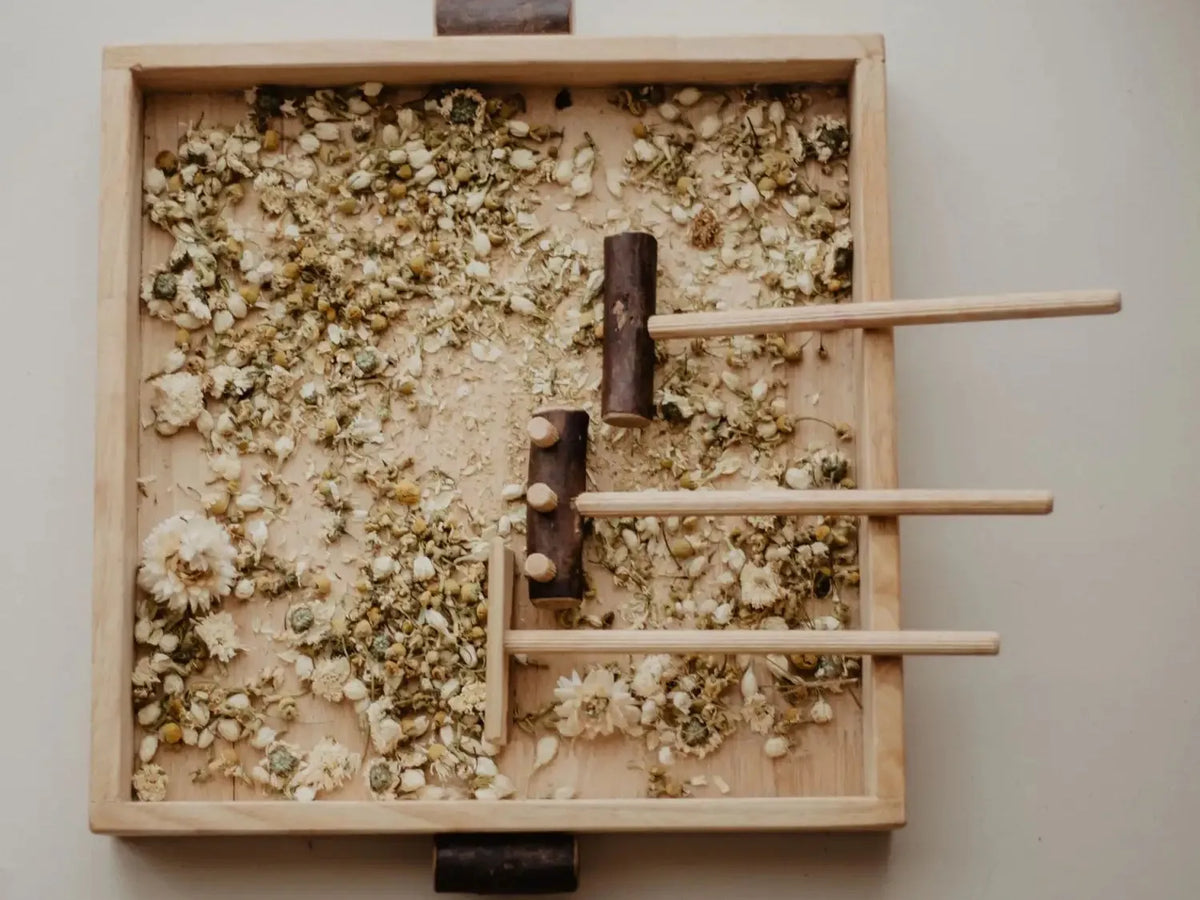 Wooden tray filled with crushed herbs and wooden sticks arranged in a pattern.