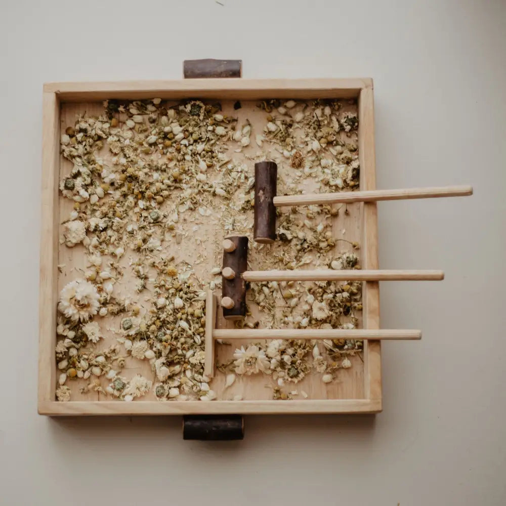 Wooden tray filled with crushed herbs and wooden sticks arranged in a pattern.