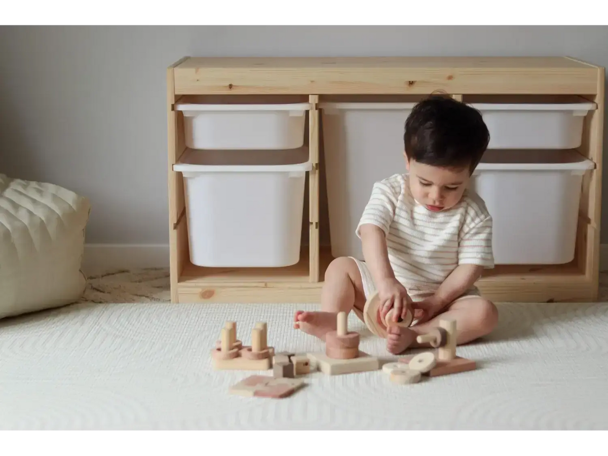 Child sitting on a carpet playing with wooden toys.