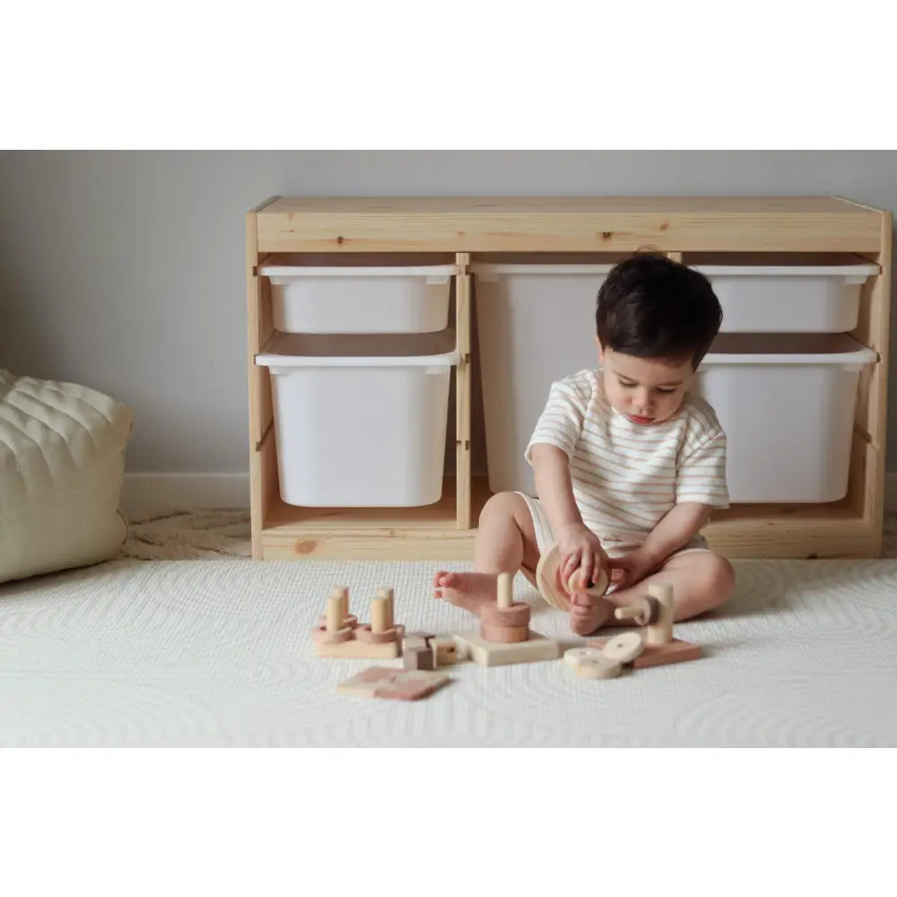 Child sitting on a carpet playing with wooden toys.