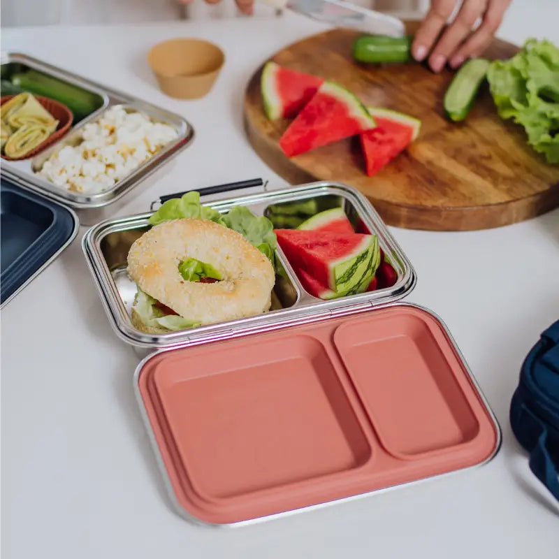 Compartmentalized lunch containers filled with various foods like sandwiches, watermelon, and rice.