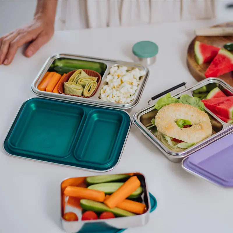 Bento-style lunch boxes filled with various healthy foods and snacks.