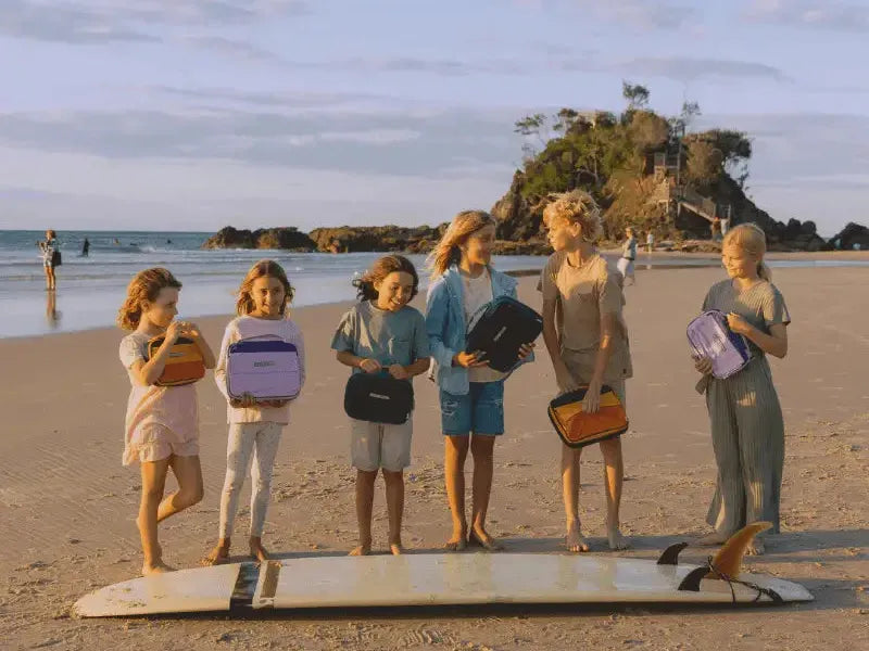 Group of young women standing on a surfboard on a beach.