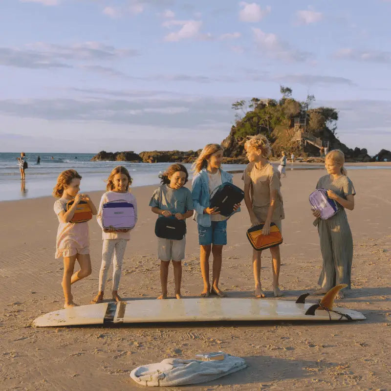 Group of young women standing on a surfboard on a beach.