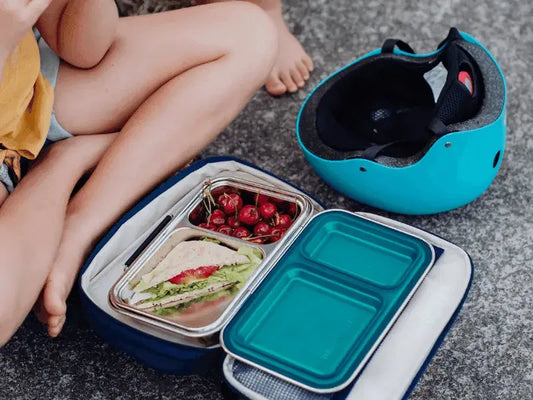 Lunchbox containing a sandwich and cherries, with a separate turquoise container nearby.