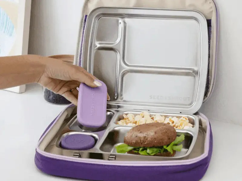 Compartmentalized lunchbox with purple exterior and stainless steel interior sections containing various food items.