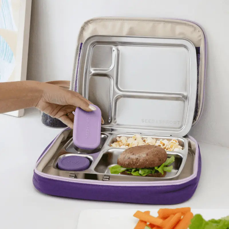 Compartmentalized lunchbox with purple exterior and stainless steel interior sections containing various food items.