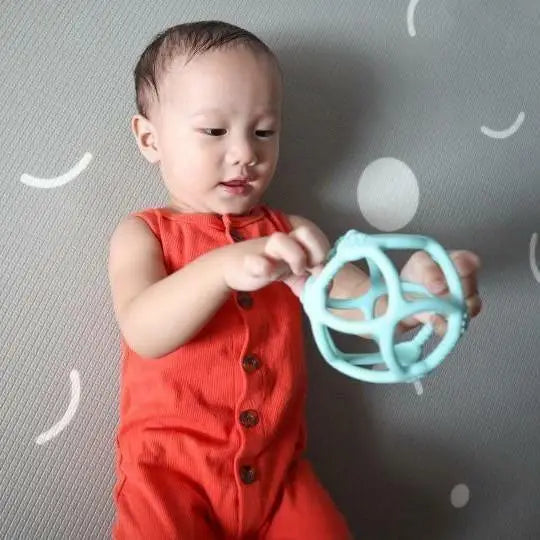 Baby in a red sleeveless outfit holding a light blue teething toy.