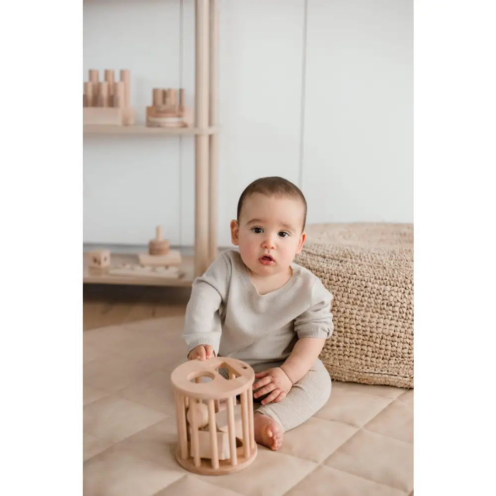 Baby sitting on the floor playing with a wooden toy.