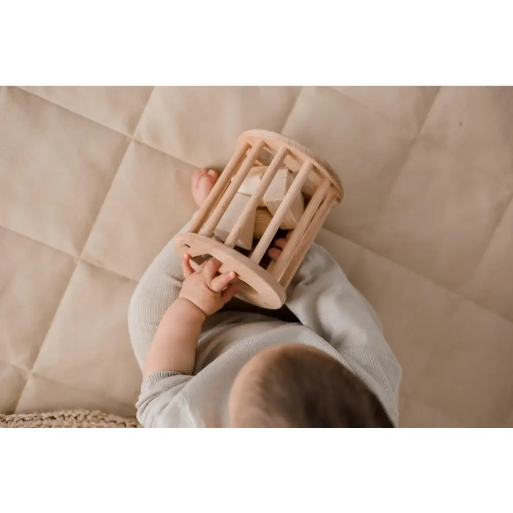 Wooden cylindrical cage or rattle held by small hands.