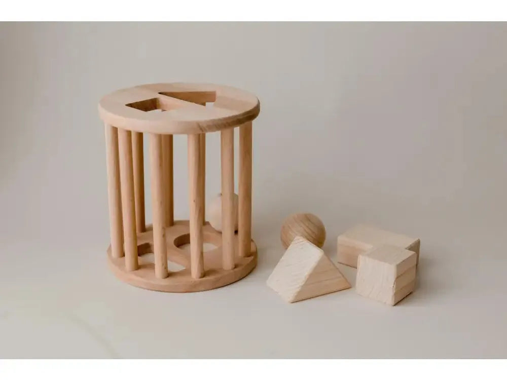 Wooden cylindrical shape sorter toy with vertical slats and geometric blocks.