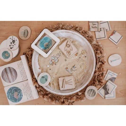 Circular tray filled with sand and various small objects arranged on its surface.