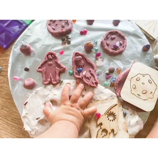 Playdough or clay surface with various cookie cutters, candies, and a child’s hand visible.
