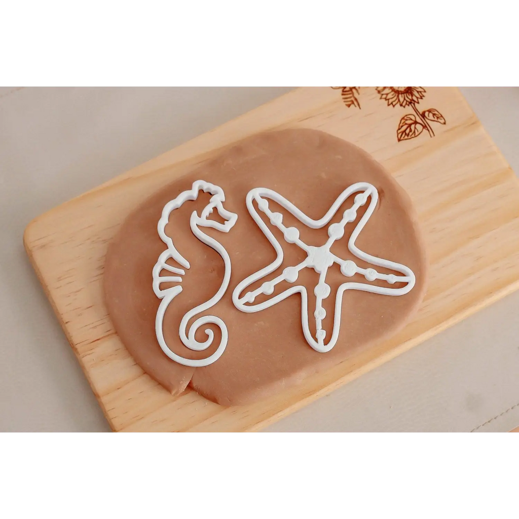 Cookie cutters shaped like a seahorse and a starfish on a wooden board.