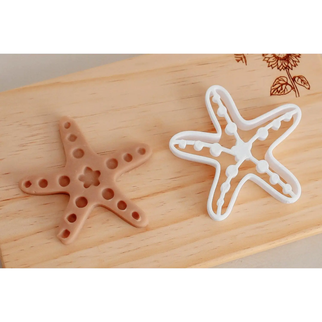 Two starfish-shaped cookie cutters, one brown and one white, on a wooden surface.