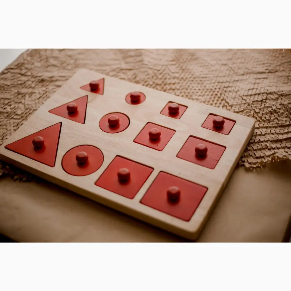 Wooden shape sorter toy with red geometric cutouts and matching pegs.