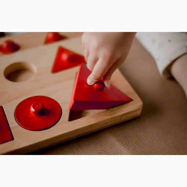 Wooden shape-sorting toy with red geometric pieces.